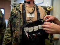 Ein Soldat trägt eine Brusttasche mit Kabeln und Technik um den Hals