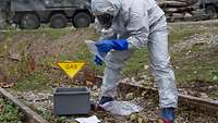 In a protective suit, CBRN defense soldiers examine an object