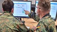 Zwei Soldaten sitzen vor einem Computer und einer zeigt auf den Bildschirm.