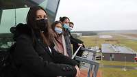 Vier Besucher mit Mund-Nasenschutz stehen auf der Aussichtsfläche des Flugtowers.