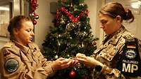 Zwei Soldatinnen stehen neben einen Weihnachtsbaum und schmücken diesen