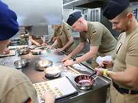 Mehrere Soldatinnen und Soldaten stehen in der Kombüse beim Plätzchen backen