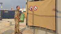 Ein Soldat trägt eine Gasflasche und steht vor einem Gefahrgutcontainer.