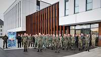Eine große Gruppe von Soldaten in Flecktarnuniform steht in Reihen vor einem mehrstöckigen Bürogebäude.