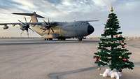 Ein mit roten und goldenen Kugeln geschmückter Weihnachtsbaum steht auf dem Rollfeld, dahinter ein A400M