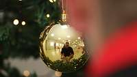 Eine goldene Christbaumkugel in der sich ein Soldat mit Weihnachtsmütze spiegelt