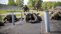 Mehrere Soldaten kriechen am Boden unter einem Hindernis