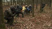 Mehrere Soldaten knien im Wald und schießen scharf