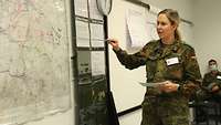 Eine Soldatin steht an einer Landkarte und berichtet etwas.