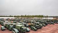 Viele militärische Fahrzeuge (Lkw, Pkw) stehen auf einer freien Fläche eng neben- und hintereinander.