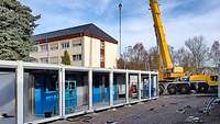 Ein großer Kran hebt einzelne Container-Baumodule auf einer Baustelle zu einem Gebäude zusammen