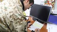Ein Soldat steht vor einem Arbeitsplatz und unterzeichnet ein Papier