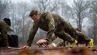 Mehrere Soldaten in Sportanzug machen draußen auf dem Sportplatz Liegestütze. 