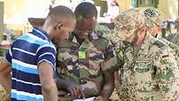 Ein malischer Soldat deutet auf ein Blatt Papier, ein deutscher Soldat und ein ziviler Malier schauen ihm über die Schulter