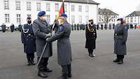 Ein Soldat übergibt eine Fahne einem anderen Soldat. Mehrere Soldaten sind zusätzlich zu sehen.