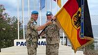 Zwei Soldaten stehen sich gegenüber und halten gemeinsam einen Flaggenstock in der Hand