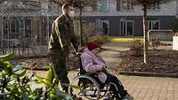 Ein Soldat begleitet eine Bewohnerin der Einrichtung bei ihrer Spazierfahrt mit dem Rollstuhl.