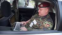 Ein Soldat sitzt in einem Auto und hat einen Laptop auf dem Schoß.