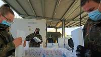 Eine Soldatin und zwei Soldaten bereiten den Versand der Corona-Impfstoffe vor.