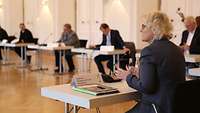 The Federal Minister of Defense and other participants conversing in a large conference room while practicing social distancing