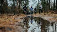 Teilnehmer eines Laufes rennen im Wald auf einen spiegelnde Pfütze zu