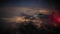 Ein Eurofighter fliegt mit Betankungsschlauch bei Nacht über eine beleuchtete Stadt.