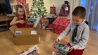 Ein Mädchen und ein Junge packen Geschenke aus.