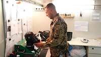 Ein Soldat steht an einem Arbeitstisch und prüft eine Atemschutzmaske