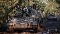 Two howitzers are driving along a muddy path through the woods.