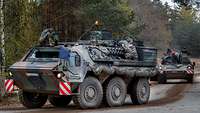 Two combat vehicles are making a turn on a paved road.