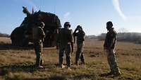 Five Hungarian gunners standing behind a PzH 2000 self-propelled howitzer with a red flag on its turret.