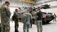 Several soldiers are standing in a large concrete hangar, with a self-propelled howitzer as a training gun behind them.