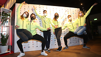 Frauen und Männer in grüngelben Sportbekleidung posieren artistisch für ein Gruppenfoto