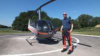 Der Pilot steht auf einer Landeplattform für Hubschrauber. Er trägt eine Sonnenbrille und ein Polohemd mit Arbeitshose.