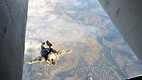 Ein Fallschirmspringer springt aus einem Flugzeug und schwebt über der Landschaft.