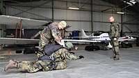 Ein Soldat mit Sprungausrüstung liegt auf einer Plane. Neben ihm prüft ein Soldat die Ausrüstung.