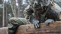 Ein Soldat im Flecktarnanzug und Helm klettert über eine Holzwand.