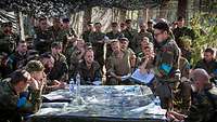 Eine Gruppe Soldaten versammelt sich um einen Tisch mit Landkarte. Über ihnen hängt ein Tarnnetz.