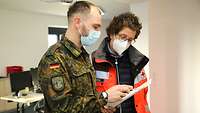Ein Soldat mit Zettel in der Hand und eine Sanitäterin stehen zusammen und besprechen sich.