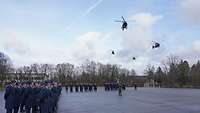 Viele Soldatinnen und Soldaten sind angetreten und schauen in die Luft. Vier Hubschrauber fliegen über sie.