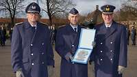 Drei Soldaten stehen in blauer Uniform nebeneinander. Der in der Mitte hält seinen Bestpreis in die Kamera.