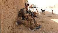 Ein Soldat sitzt an einer Wand und beobachtet aufmerksam eine Straße in einer malischen Ortschaft 