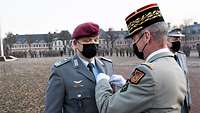 Ein französischer Soldat steckt einem deutschen Soldaten einen Orden an die linke Brust.