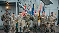 Sieben Soldaten aus vier Ländern stehen vor den Flaggen und Wappen der EFP-Battlegroup