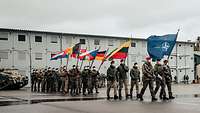 Zahlreiche Soldaten marschieren mit Flaggen in Formation auf einem Platz.