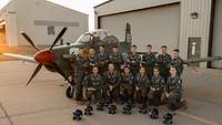 Pilotenschülerinnen und -schüler der Klasse 22-06 posieren in ihren Fliegerkombis für ein Gruppenfoto vor einer T-6.