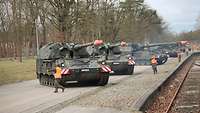 Mehrere Panzerhaubitzen stehen an einem Bahndamm