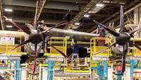 Fünf Männer in einer Produktionshalle montieren ein schweres Metallbauteil an Flugzeugtragflächen.