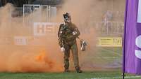 Ein Soldat steht in einem Stadion, von seinem Bein steigt orangefarbener Rauch auf.