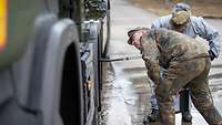 Ein Mann in Uniform guckt unter einen LKW